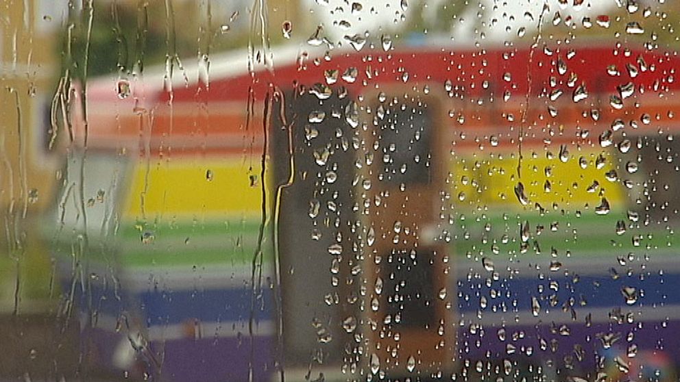 Regnbågsfärgad husvagn sedd genom ett regnvått fönster.