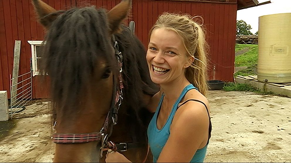 tjej med blont hår och hästsvans bredvid häst utanför ladugård