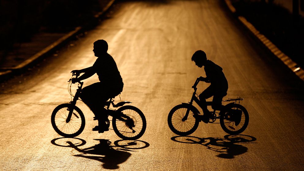 Två ungdomar cyklar på gata i motljus