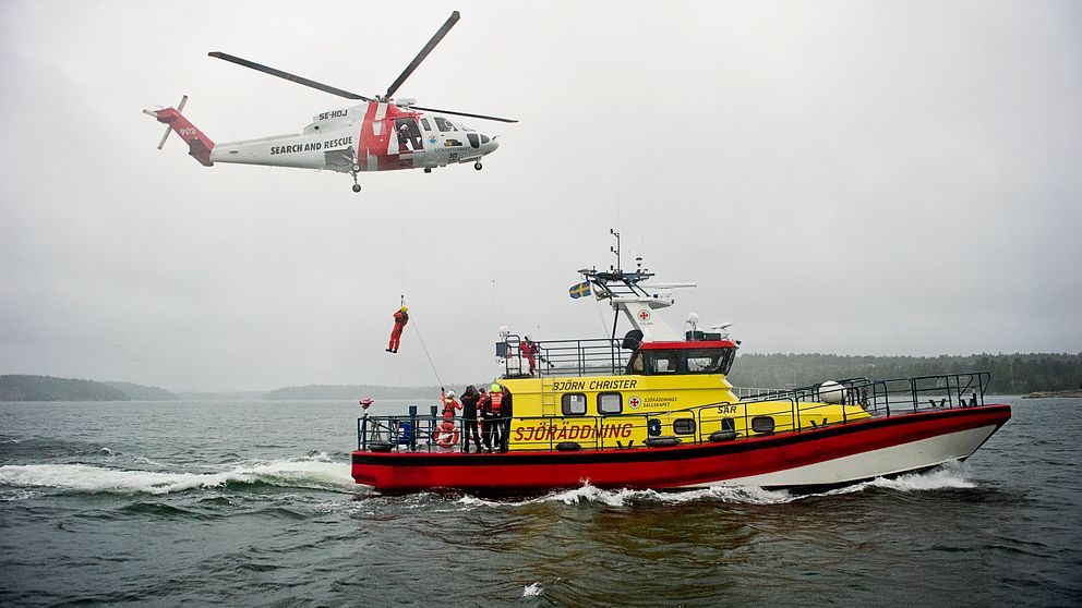 Sjöräddningssällskapets båt ute på vatten. Ovanför flyger en helikopter.