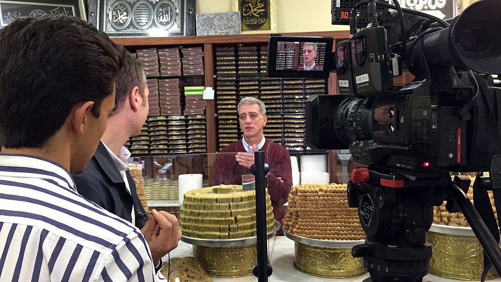 Salim Sakka vid konditoridisken med tårtfat av baklava staplade på varandra.