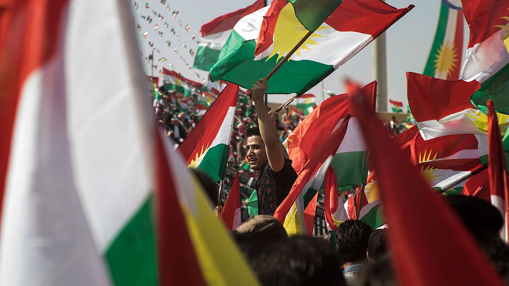 Man omgiven av kurdiska flaggor.