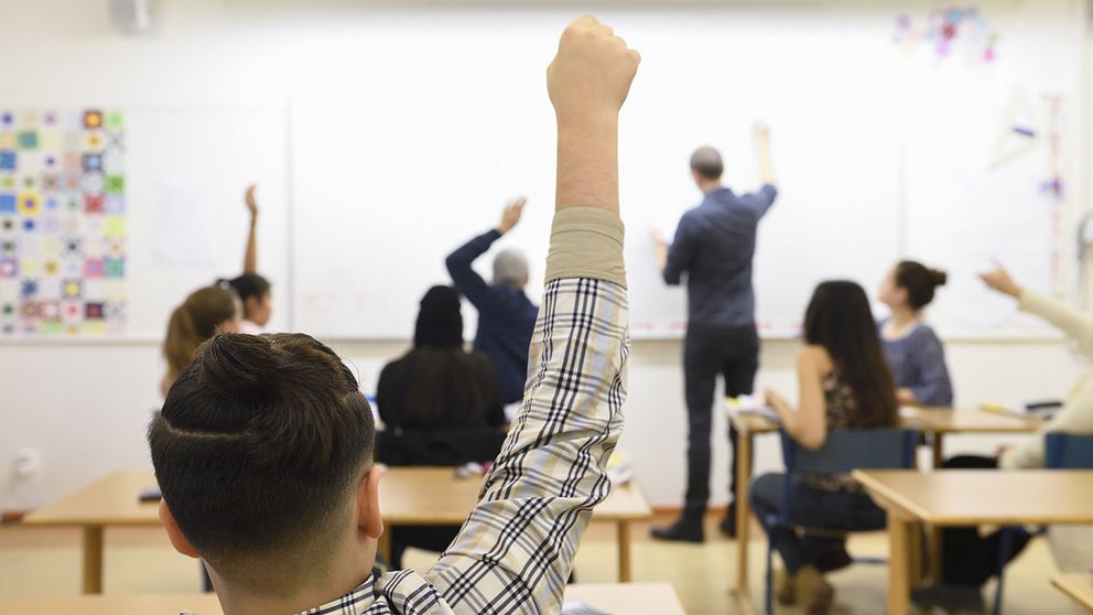 En elev räcker upp handen i ett klassrum.