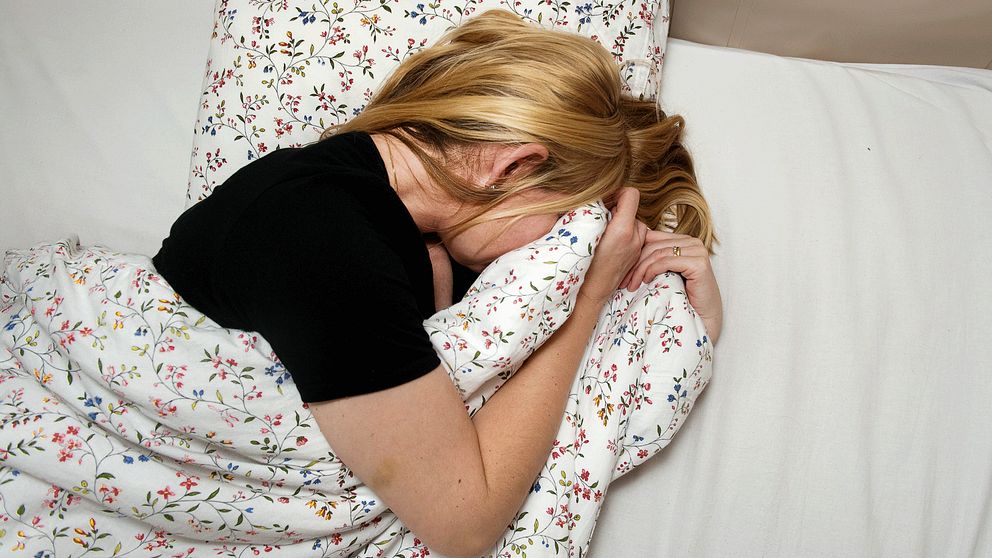 Kvinna på säng gömmer huvudet i täcket