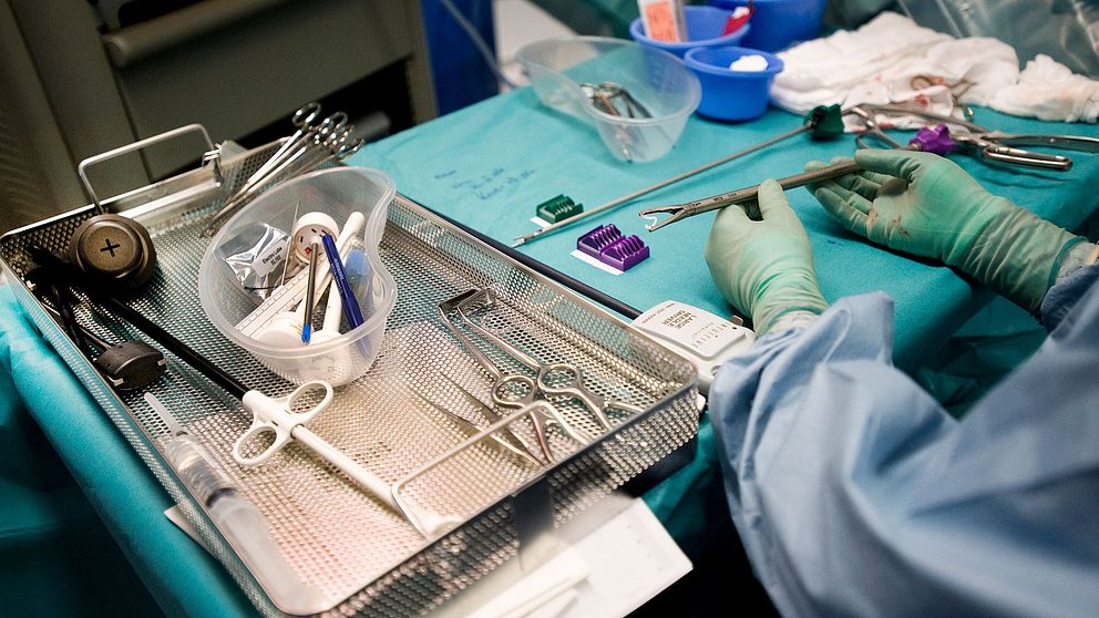 Ett bord med verktyg i en operationssal. En läkares händer iförda gröna plasthandskar håller i ett verktyg.