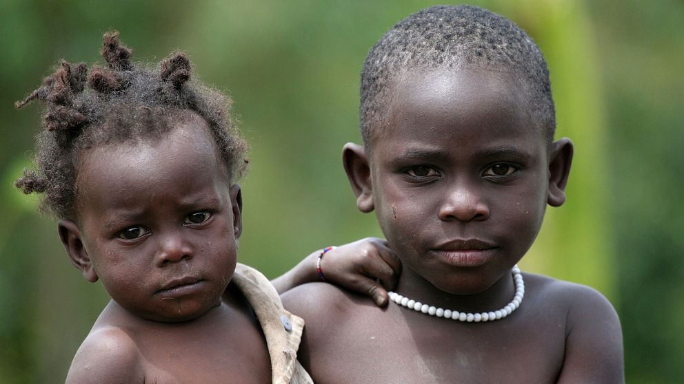 En flicka bär sin yngre syster på armen i en by i västra Uganda. Bland de ”osynliga”, som främst lever i Afrika och Asien, är mer än en tredjedel barn som inte har registrerats vid födseln.