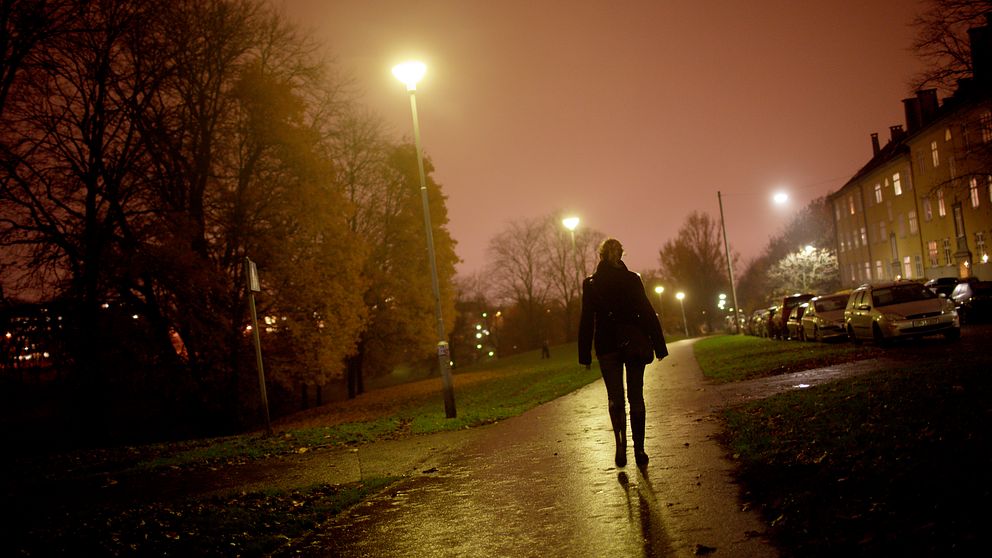 Kvinna går på gångväg i ett mörkt bostadsområde. Lampor lyser upp vägen.