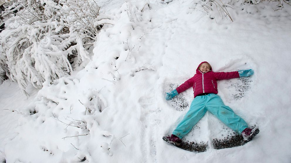 En flicka ligger ner i snön och gör en snöängel.