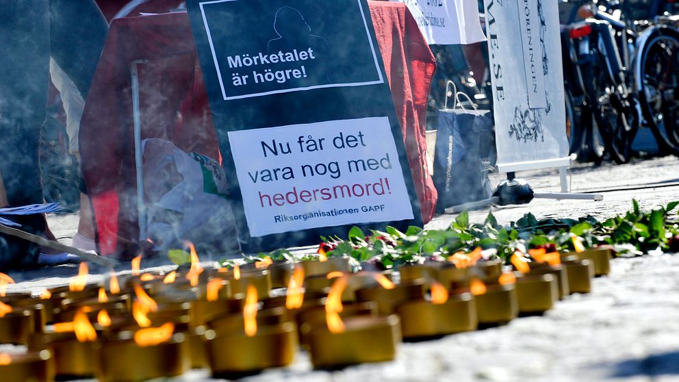 En mängd marschaller brinner i förgrunden. I bakgrunden finns en skylt med texten ”Mörkertalet är högre! Nu får det vara nog med hedersmord”.