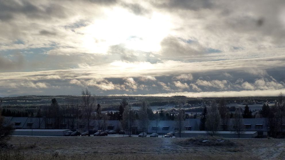 Vybild över bygd med frost som täcker marken. Solen tittar fram mellan grå moln.