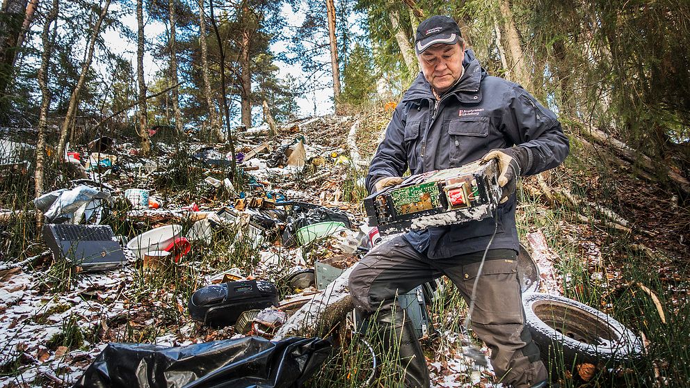 Naturbevakaren Anders Berglund står bland mängderna av sopor som har slängts i naturreservatet. I handen har han lyft upp en gammal dator.