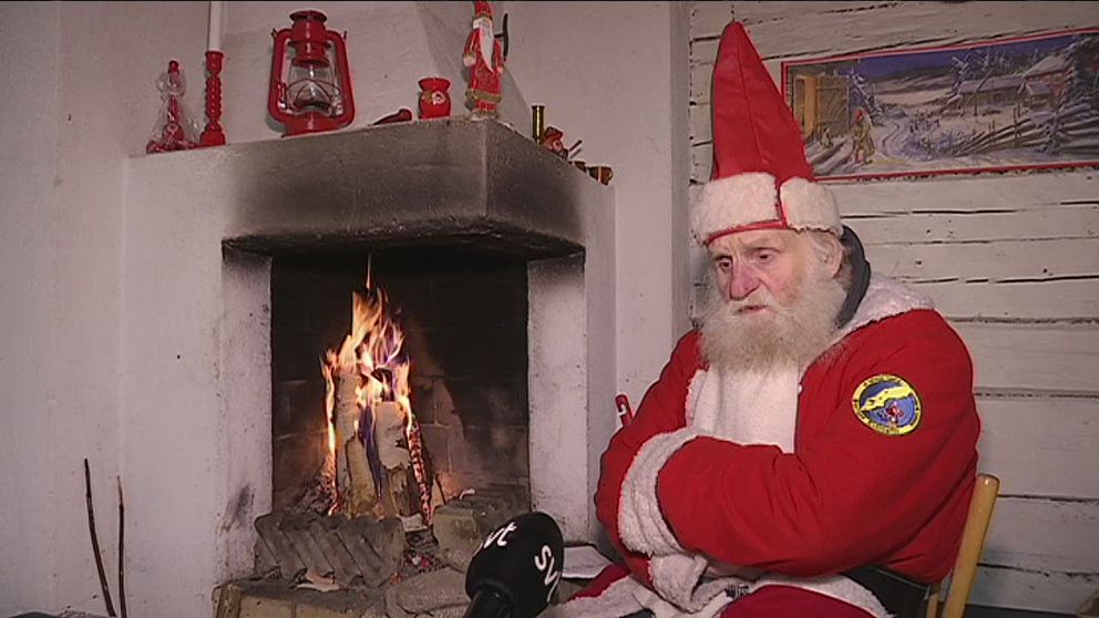 en äldre man utklädd till tomte som sitter deppig vid öppen spis