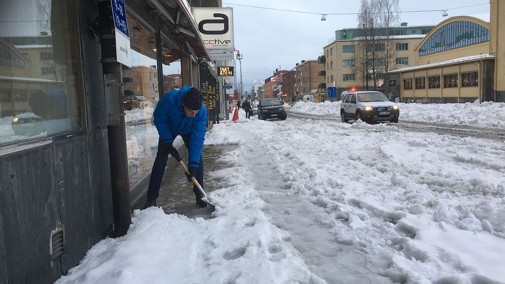Man skottar bort snö o vatten vid port på Kungsgatan Luleå