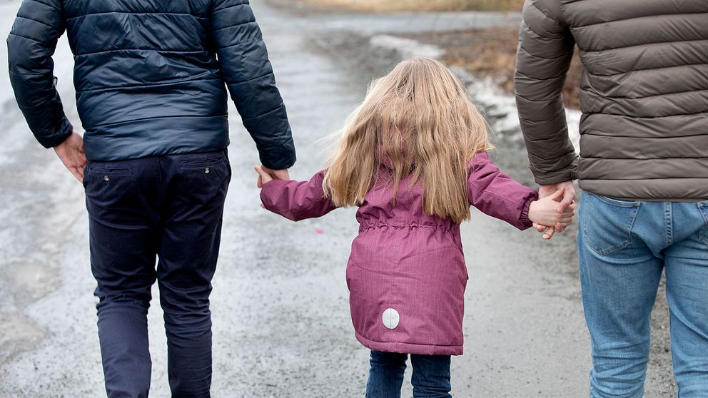 Två pappor går hand i hand med sin dotter