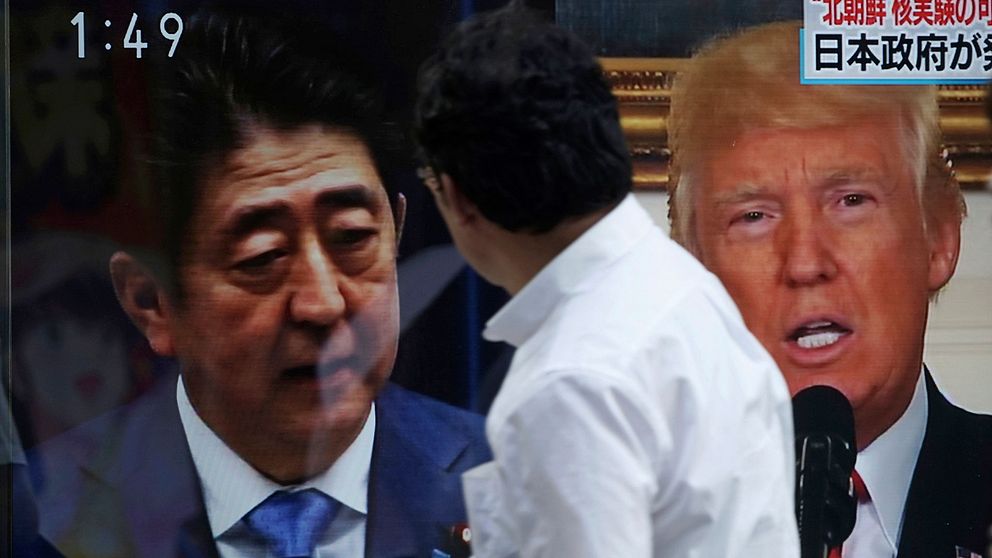 En man framför Shinzo Abe och Donald Trump på skärmar i Tokyo