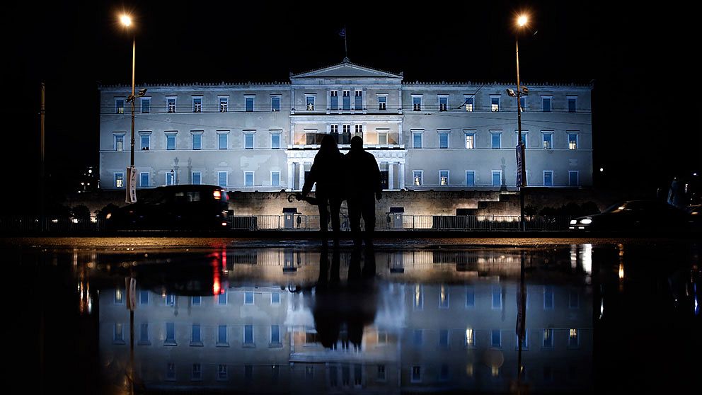 The illuminated Greek Parliament building ahead of the Nov. 14 World Diabetes Day, is reflected on a rain-soaked pavement as a couple wait to cross a street in Athens on Monday, Nov. 11, 2013. (Petros Giannakouris)