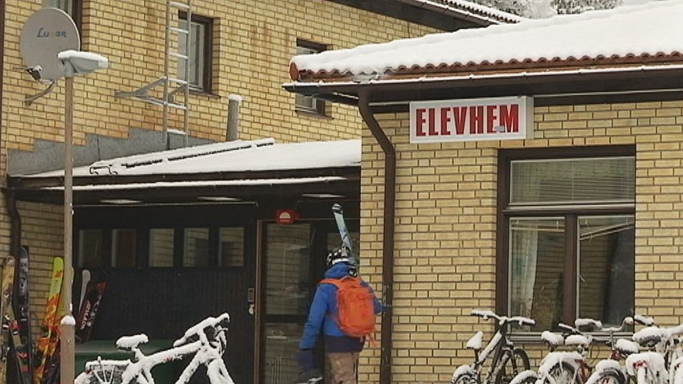 person bär skidor mot entre på byggnad med skylten ”elevhem”