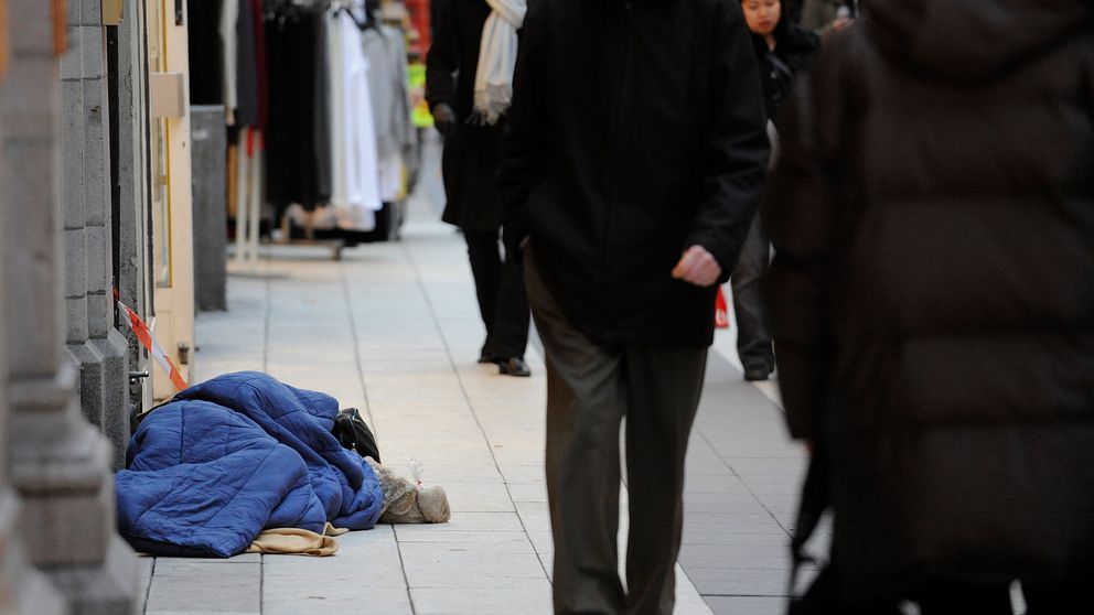 En uteliggare med en blå sovsäck sover på gatan.