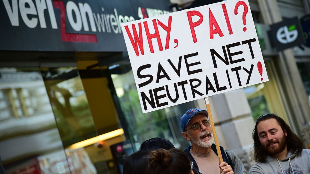 En liten grupp av människor. En person håller i en skylt med texten: Why Pai? Save net neutrality!