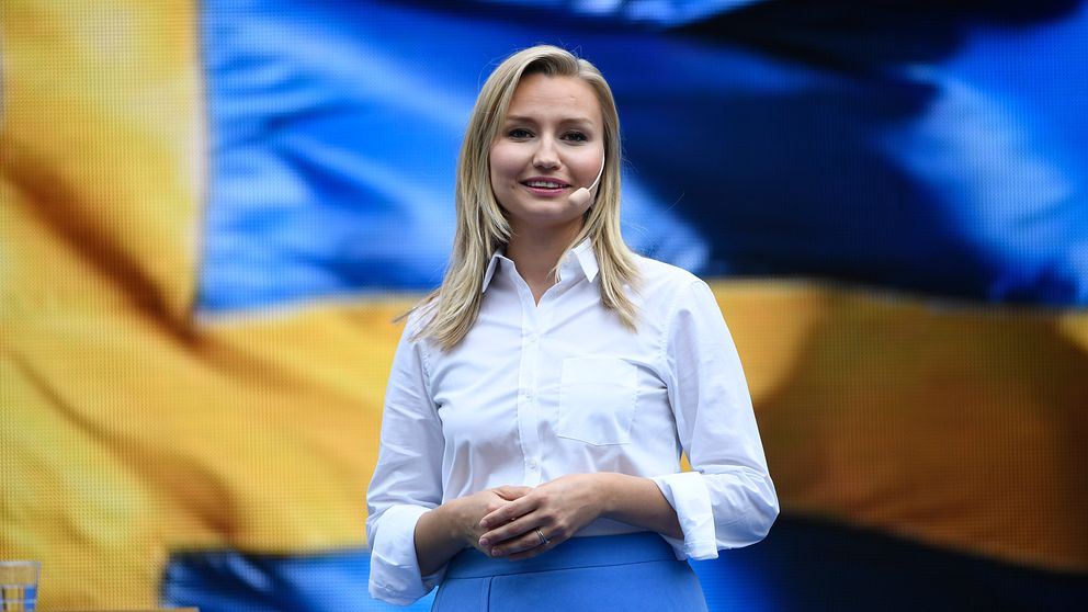 Ebba Busch Thor framför en stor svensk flagga.
