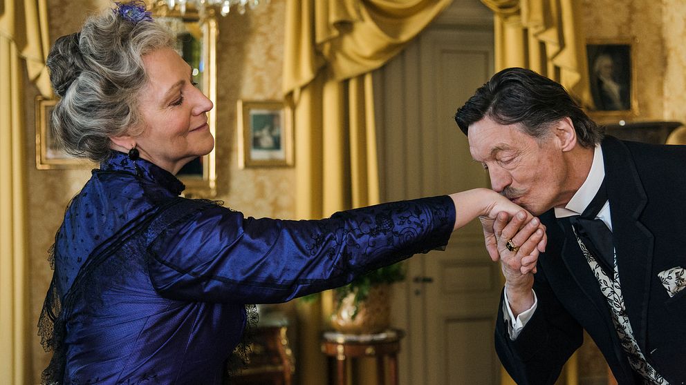 En bild en bild från tv-serien Fröken Frimans krig, där Johannes Brosts roll Sievert kysser Alma, spelad av Lena T. Hansson, på handen.