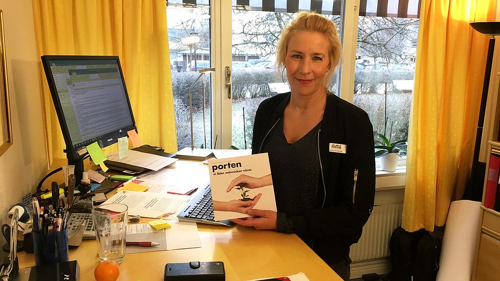 Jenny Nordansjö står i mitten av bilden, i kontorsmiljö. Hon håller upp något med ordet ”Porten” på.