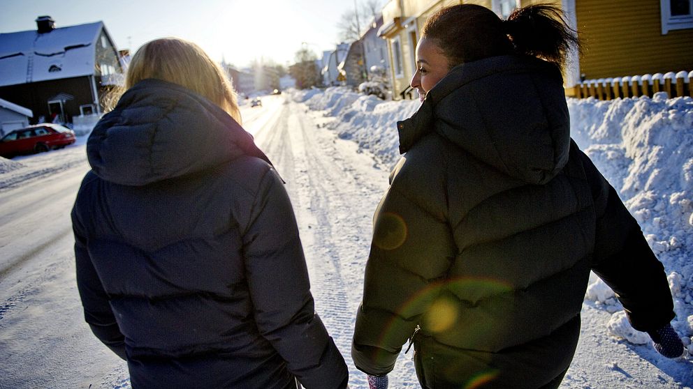 Två kvinnor går längs med solig snötäckt gata.
