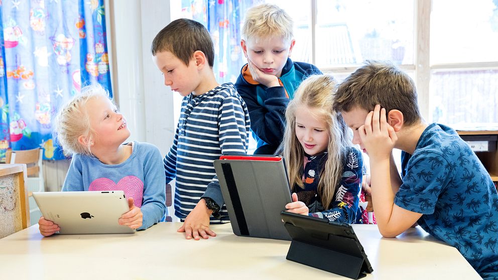 Fem skolbarn tittar på läsplattor tillsammans.