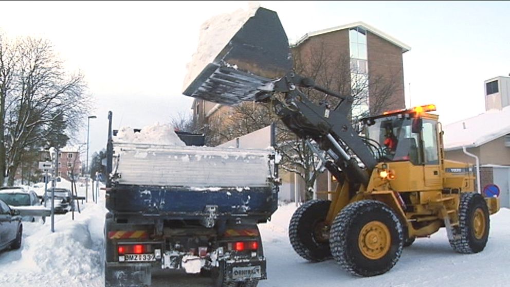 En traktor dumpar snö i ett lastbilsflak.