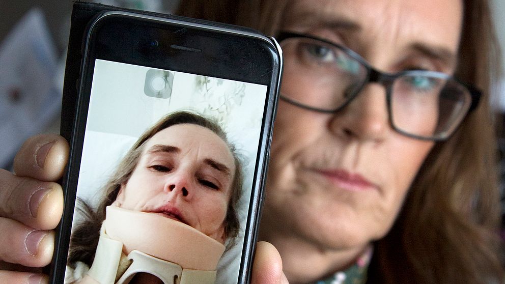 medelålders kvinna håller fram mobil för att visa bild på sig själv med nackkrage