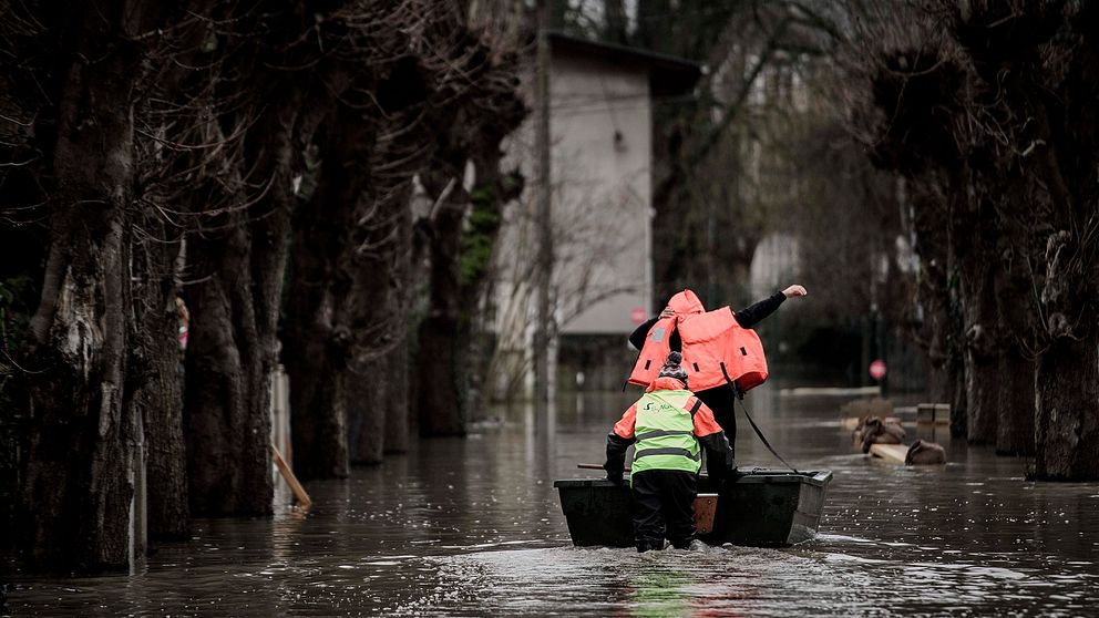 Två personer tar sig fram med båt på en översvämmad gata.