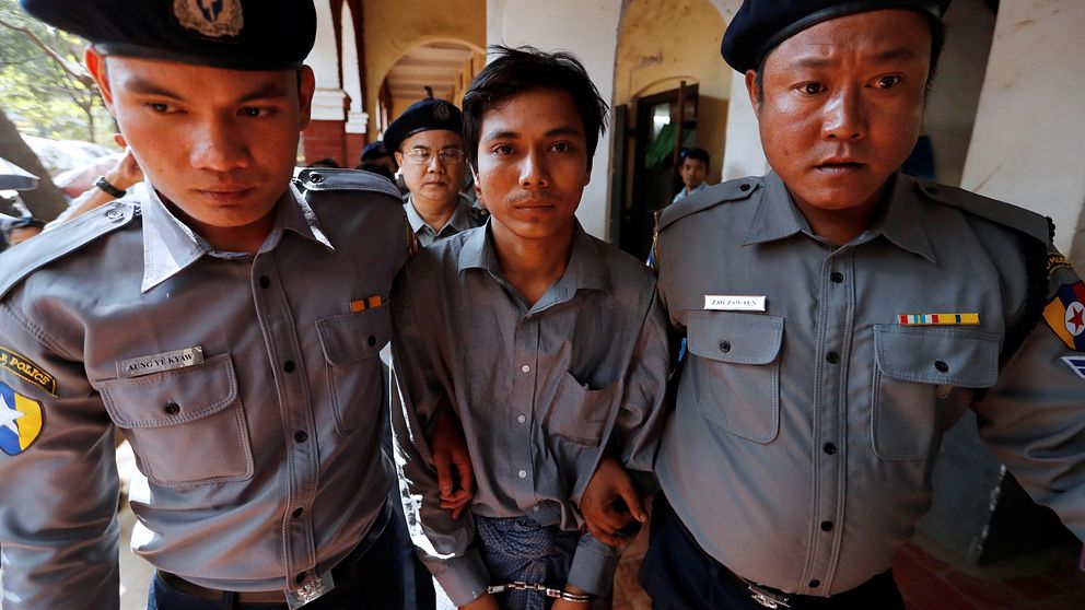 Kyaw Soe Oo har handfängsel på sig och går mellan två poliser som håller i hans armar.