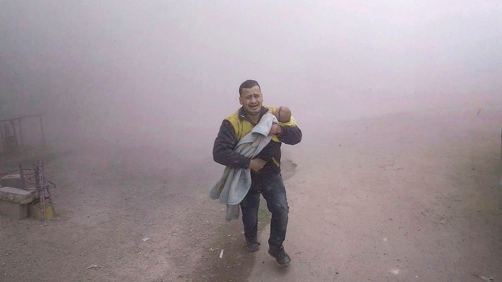 En man tillhörande Vita hjälmarna bär sin skadade son när han flyr från ett flyganfall på tisdagen.