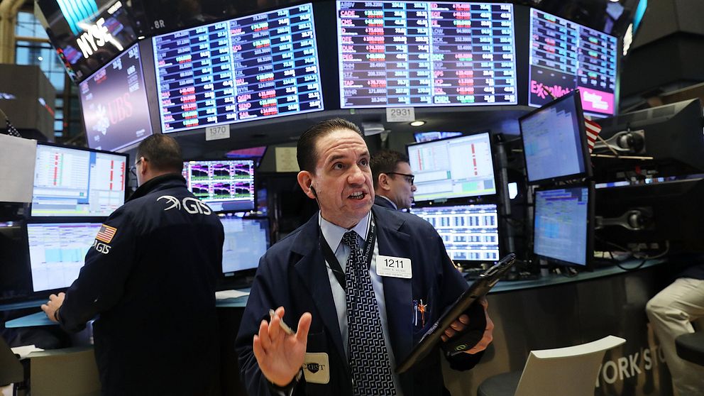 En börsmäklare i kostym står framför ett antal skärmar med börsinformation.