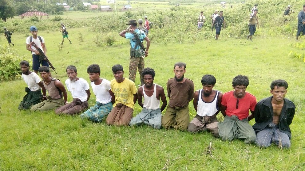 Tio burmesiska män sitter bakbundna på knä med väpnade män bakom dem håller vakt.