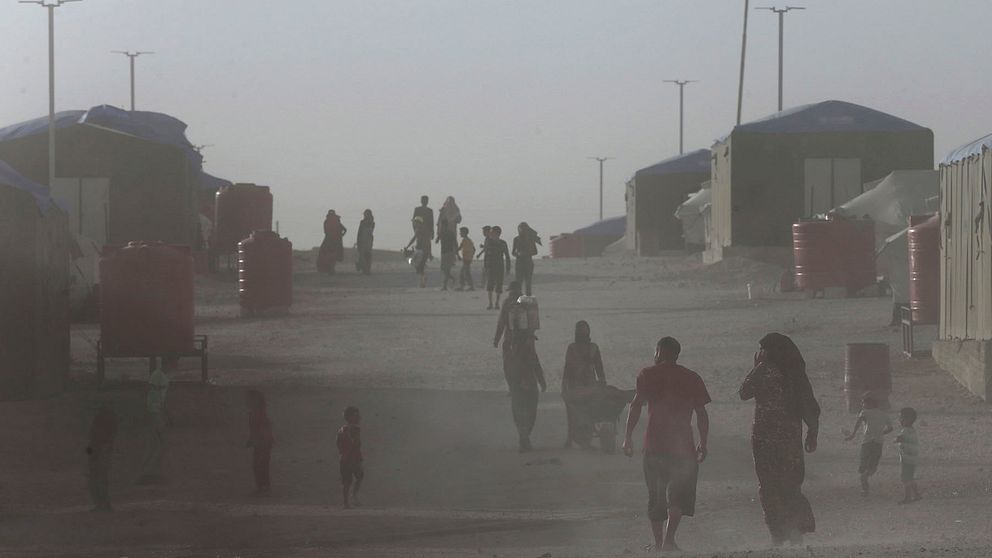 Ett dammigt läger i norra Syrien där människor går nedför en väg med tält på varje sida.