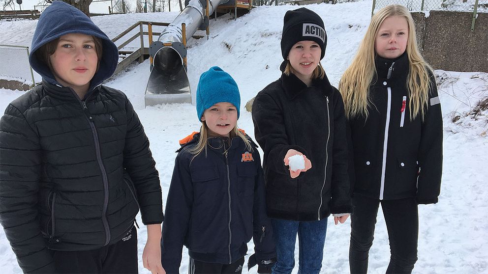 Fyra barn på skolgård med snö. Ett av barnen håller i en snöboll.