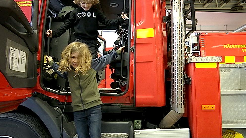 Två barn hoppar ner från förarsätet på en brandbil.