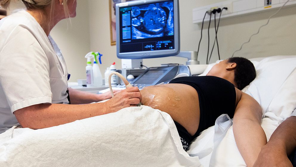 En gravid kvinna ligger i en sjukhussäng. En barnmorska undersöker kvinnans mage med ultraljud.