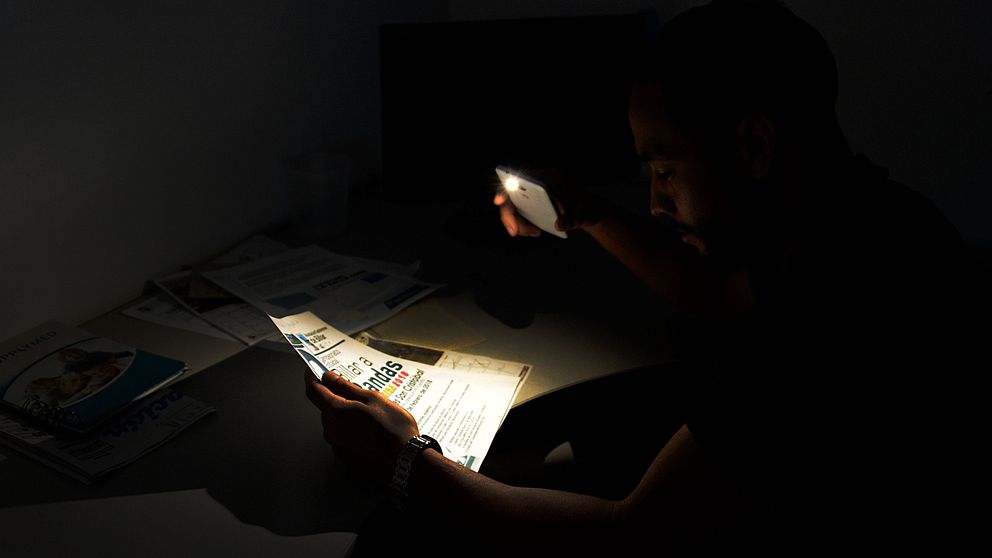 Man i Venezuela läser tidning med mobilen som ficklampa.