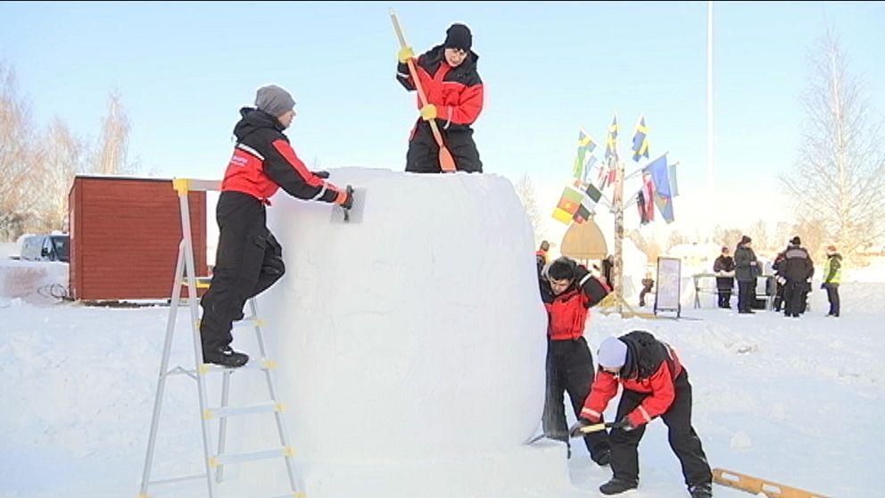 Fyra män i overaller jobbar på ett block av is och snö.