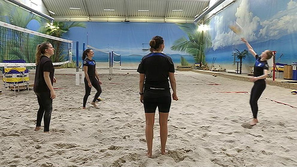 Fyra volleybollspelare tränar i en sandig inomhushall.