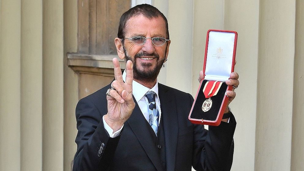 Ringo Starr håller upp sin medalj utanför kungliga slottet i London, England.