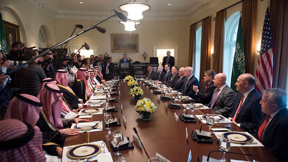 På ena sidan bordet sitter Saudiarabiens delegation, på den andra sitter USA:s delegation. På bägge sidor om bordet sitter enbart män.
