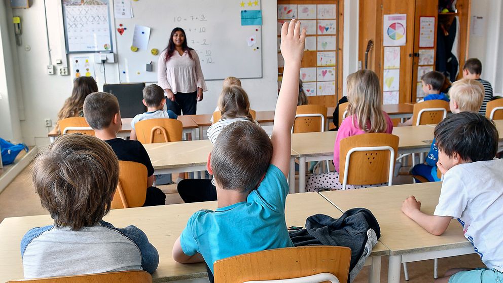ung abarn i klassrum, kvinnlig lärare framme vid tavlan