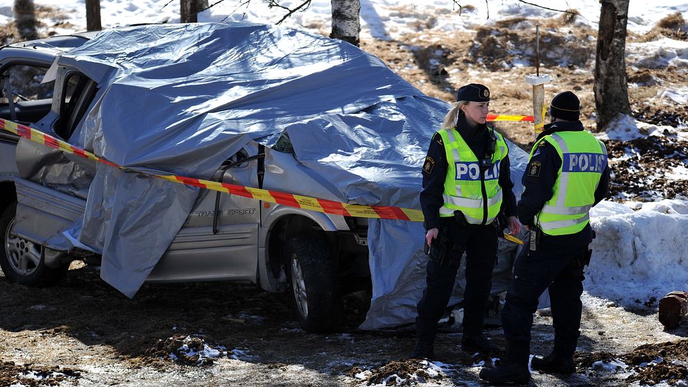 Två poliser står framför en silvrig bil som är täckt med en presenning
