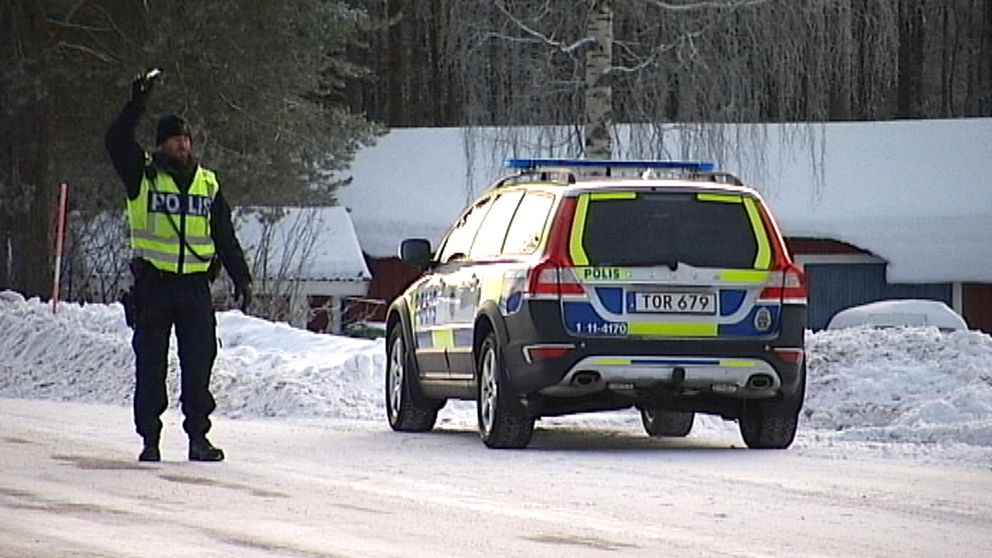 En polis med varselväst vinkar bredvid en parkerad polisbil.