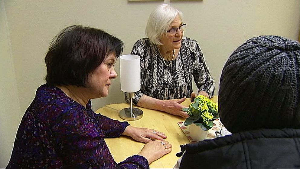 Två kvinnor från Asylkommittén vid ett bord med en asylsökande som sitter med ryggen mot kameran.
