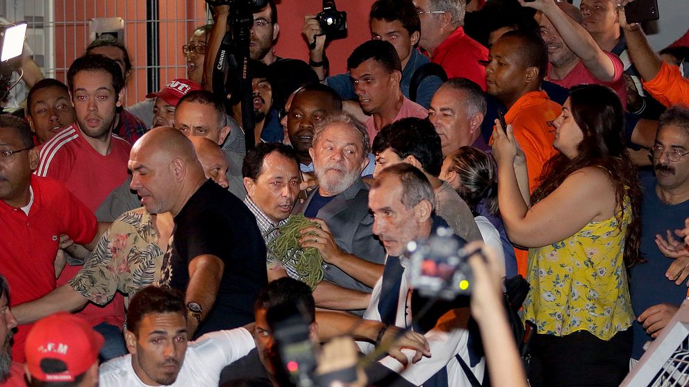 Här lämnar Lula da Silva (mannen med skägg och grå kavaj i mitten av bilden) metallarbetareförbundets högkvarter för att överlämna sig själv till polisen.