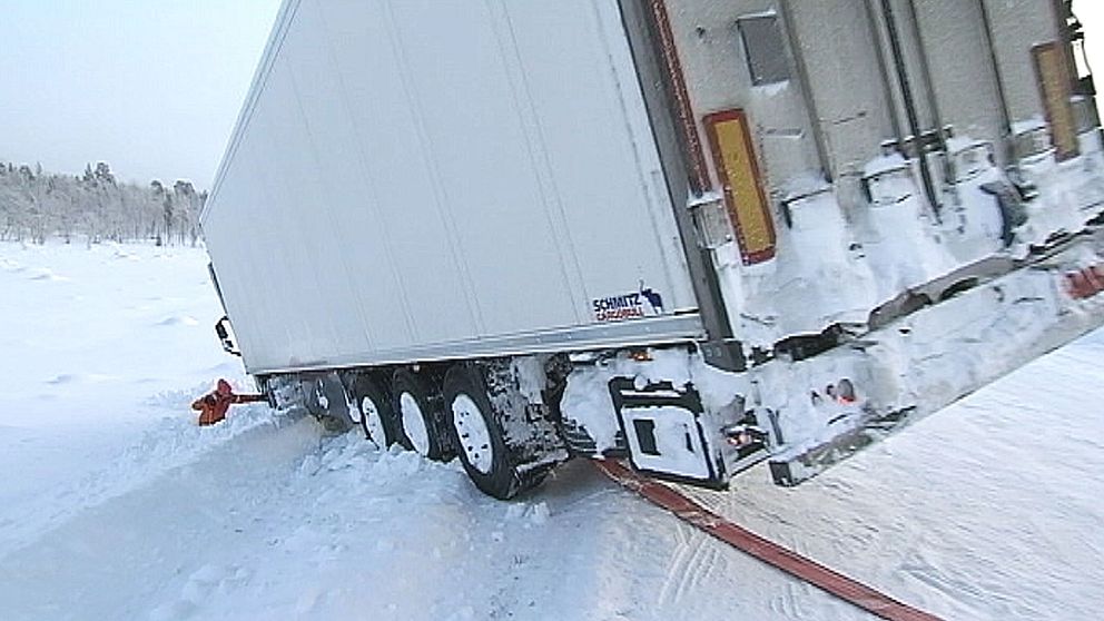 lastbilssläp som står halvvägs ner i diket på vinterväg